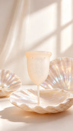 Copo menstrual GIOCUP® Pearl, translúcido, pousado numa concha nacarada com luz suave