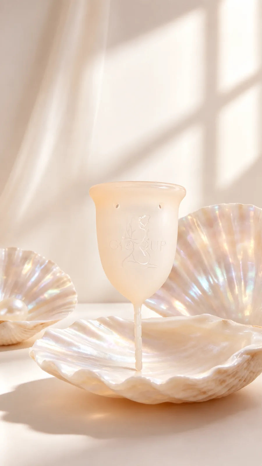 Copo menstrual GIOCUP® Pearl, translúcido, pousado numa concha nacarada com luz suave