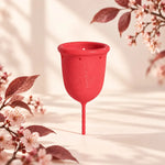 Copo menstrual GIOCUP® Rose em silicone médico, sobre fundo creme com ramos de flor de cerejeira