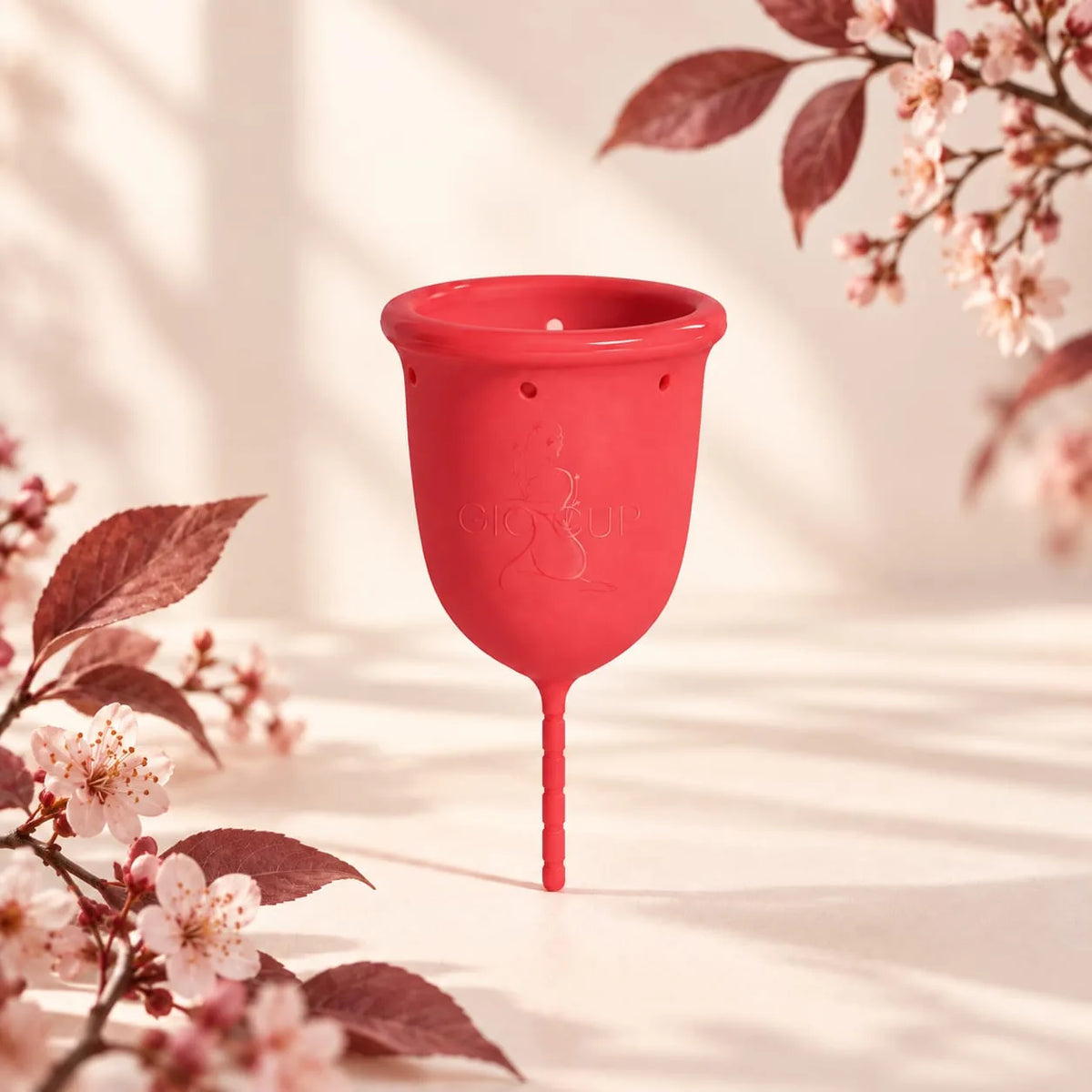 Copo menstrual GIOCUP® Rose em silicone médico, sobre fundo creme com ramos de flor de cerejeira