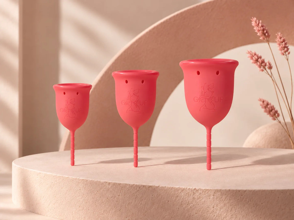 Copos menstruais GIOCUP® Rose nos tamanhos 0, 1 e 2, lado a lado sobre um pedestal