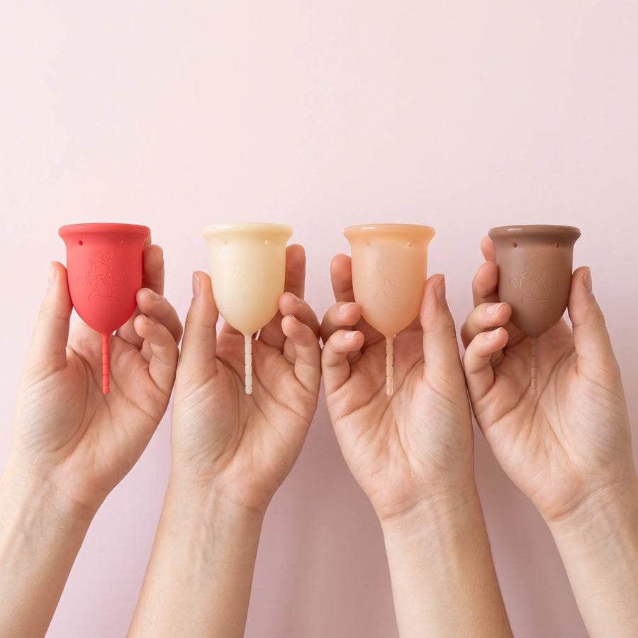 Four hands holding the GIOCUP® Rose, Pearl, Amber and Agate menstrual cups